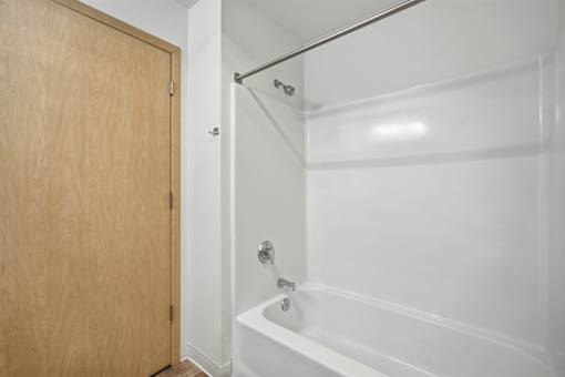 A white bathroom with a wooden door and a white bathtub.
