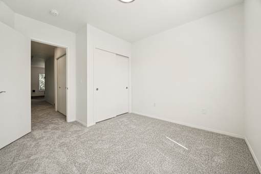 A room with white walls and carpeted floor with a doorway leading to another room.