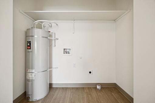 A water heater is installed in a room with white walls and wooden flooring.