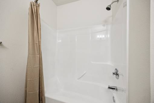 A white bathtub with a shower head and a curtain hanging on the side.