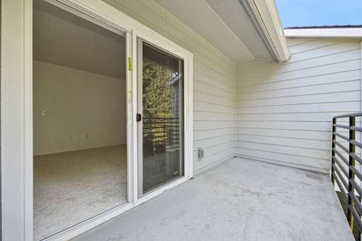 A sunny day outside a white sided house with a glass door open.