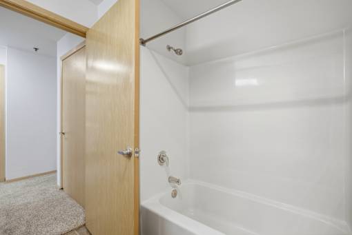 A white bathroom with a wooden door and a white bathtub.