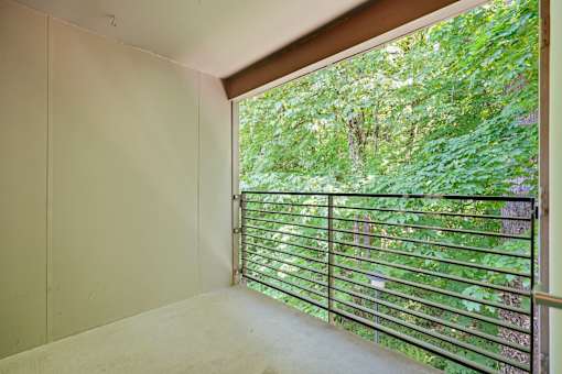 A room with a window that has a view of a green forest.