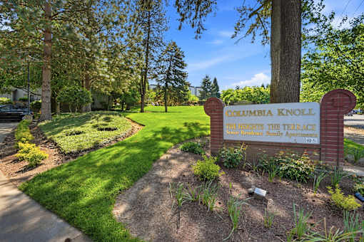 A sign for Columbia Knoll Apartments is in front of a tree.
