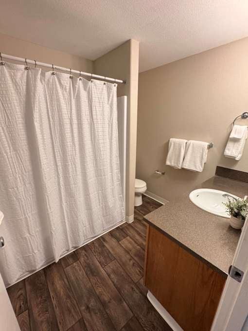 A bathroom with a white shower curtain and wooden floors.