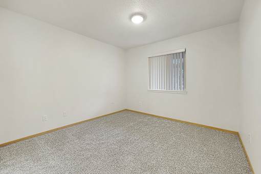 A room with a carpeted floor and a window with blinds.