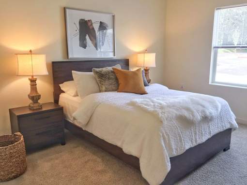 A bedroom with a bed, two lamps, and a painting on the wall.