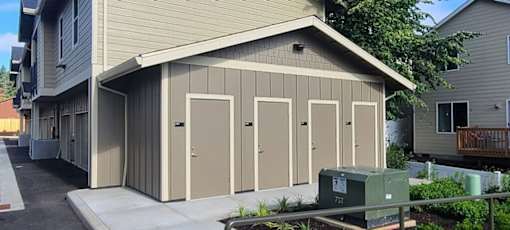 A small building with four doors is situated in front of a house.