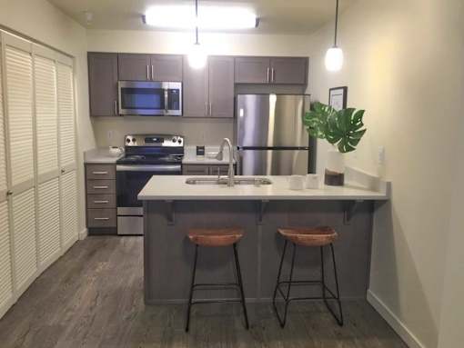 A kitchen with a refrigerator, stove, and bar stools.