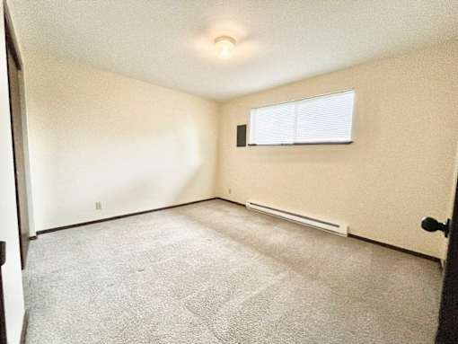 A room with a carpeted floor and a window with blinds.