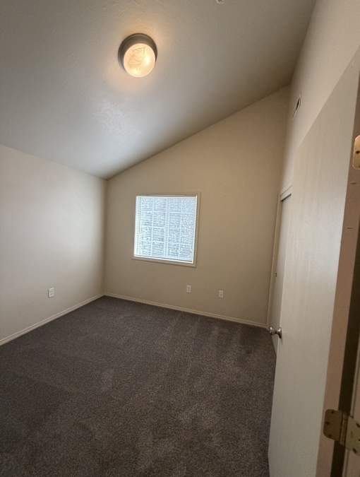 A room with a carpeted floor and a window with blinds.