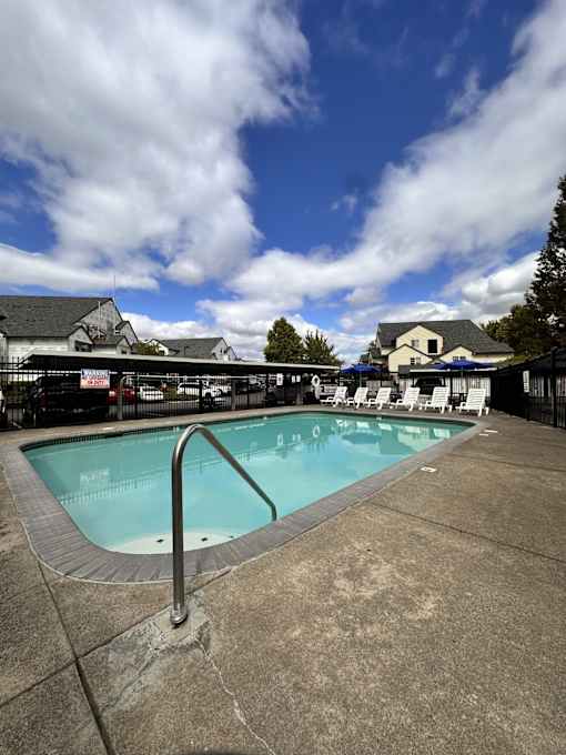 A swimming pool with a metal ladder and a cloudy sky.