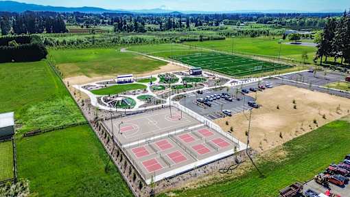 An aerial view of a sports complex with a basketball court, tennis courts, and a parking lot.