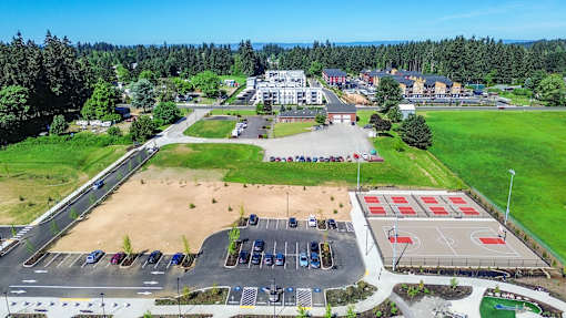 A large outdoor basketball court is surrounded by a parking lot and buildings.