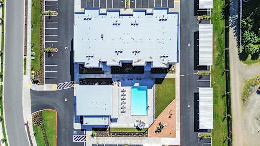 An aerial view of a large building with a parking lot and a pool in front.