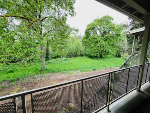 A balcony with a metal railing overlooks a green, tree-filled landscape.