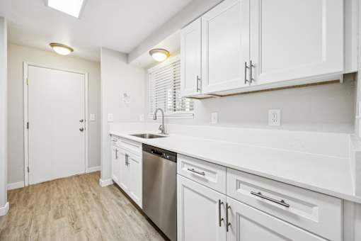 A white kitchen with wood floors and stainless steel appliances.