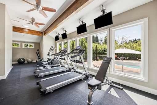 A gym with treadmills, a fan, and a view of a pool.