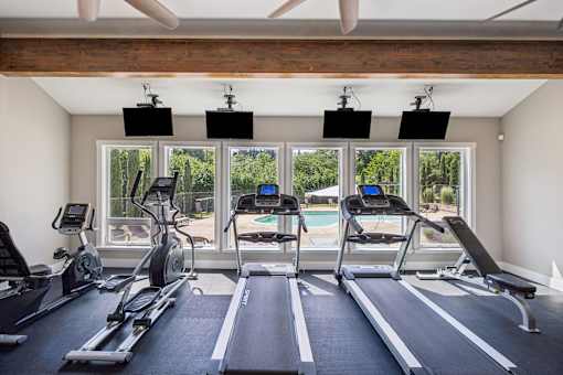 A gym with treadmills, exercise bikes, and a ceiling fan.