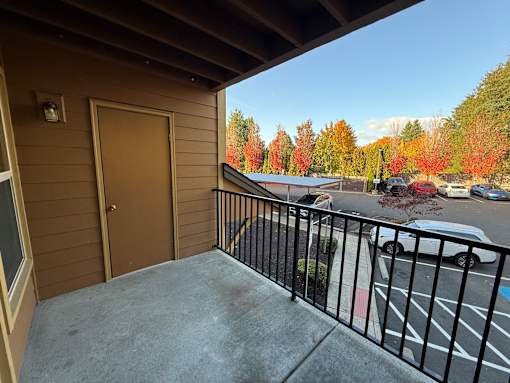 A balcony with a black railing and a view of a parking lot and trees.