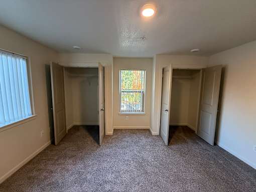 A room with carpeted floor and a window with blinds.
