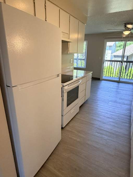 A white refrigerator is in a kitchen with wood flooring.