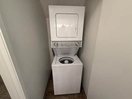 A white toilet with a built-in washing machine is in a small, white-walled bathroom.