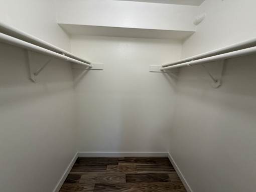 A walk in closet with a wooden floor and white walls.