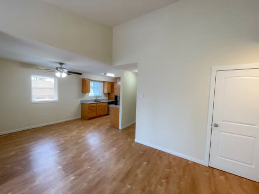 an empty living room with a kitchen in the background