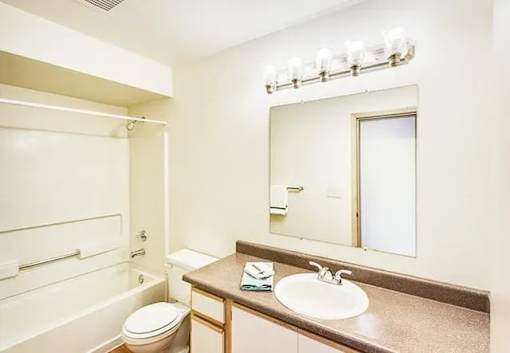 A bathroom with a toilet, sink, and mirror.
