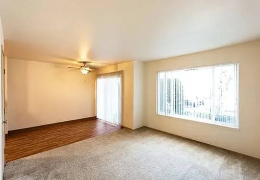 A room with a ceiling fan and a window with a view of a cityscape.
