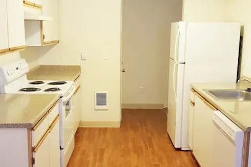 A kitchen with white appliances and wooden floors.