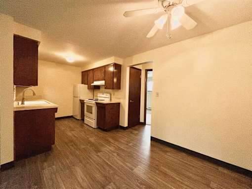A kitchen with a white ceiling fan and wooden floors.