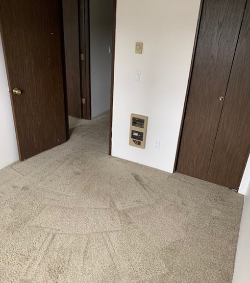 A carpeted hallway with a door on the left and a wall-mounted thermostat on the right.