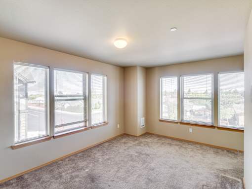 A room with a carpeted floor and three windows.