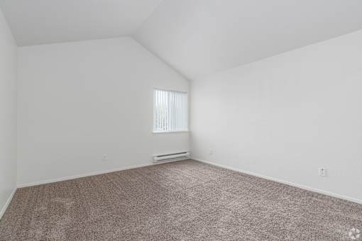 A room with a carpeted floor and a window with blinds.