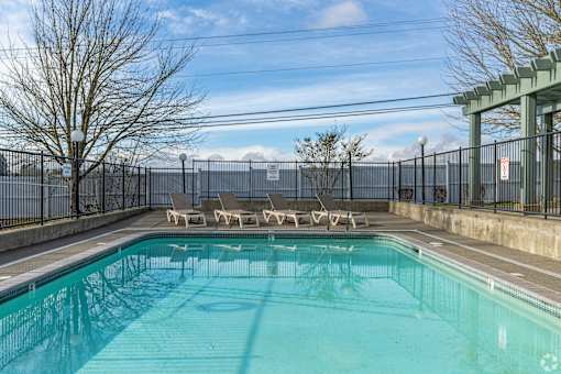 A pool surrounded by a fence with sun loungers on the side.