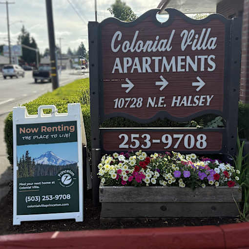 A sign for Colonial Villa Apartments with a phone number and a picture of a mountain.