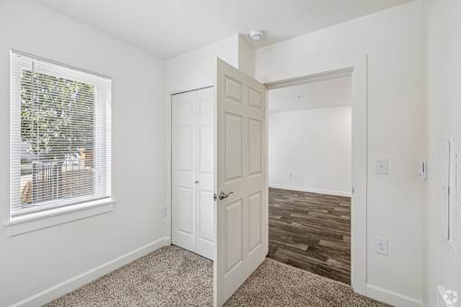 A room with a white door, a window with blinds, and a wooden floor.