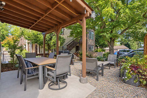 A patio with a table and chairs under a wooden roof.