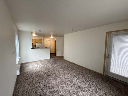 A spacious room with a carpeted floor and a small kitchenette in the corner.