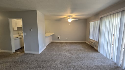 an empty living room with large windows and a ceiling fan