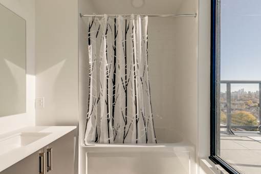 A white bathroom with a shower curtain with black branches on it.
