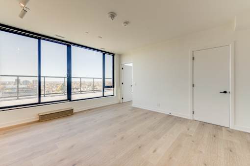 A large empty room with wooden floors and a view of the city through the windows.