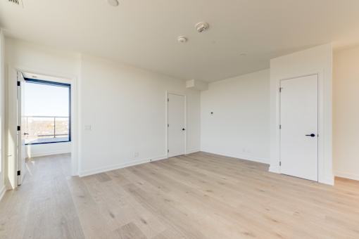 A room with white walls and wooden flooring with a door on the right.