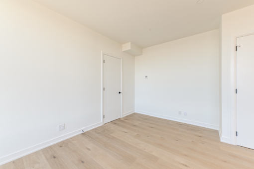 A room with white walls and wooden flooring with two doors.