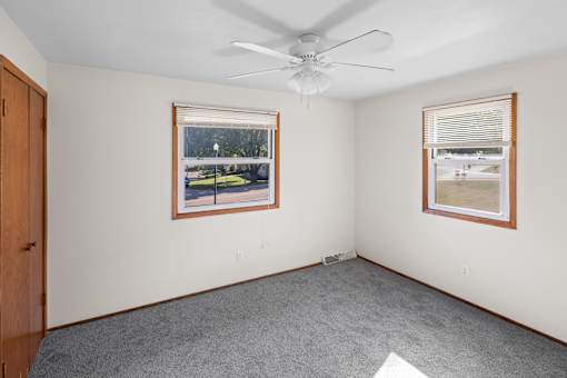 A room with a ceiling fan and two windows.