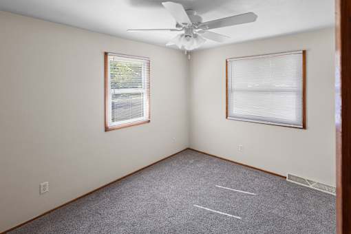 A room with a ceiling fan and two windows.