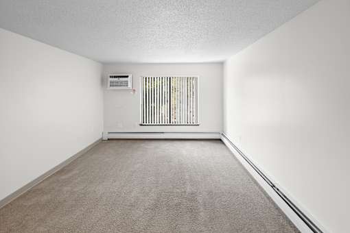 A room with a carpeted floor and a window with blinds.