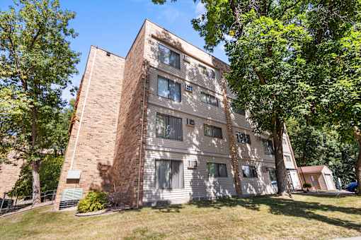 A tall building with a mix of brick and siding exterior is surrounded by trees.